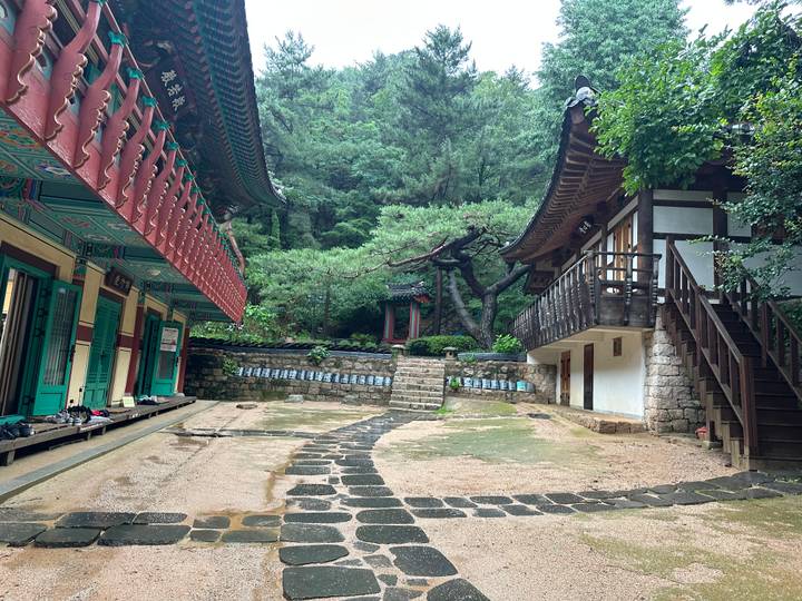 Quiet courtyard of a traditional Korean temple complex surrounded by forested hills.