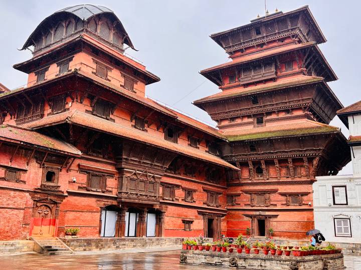 Twin red brick palace towers with tiered roofs in Kathmandu Durbar Square under light rain.