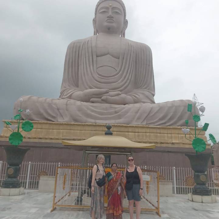 Visitors stand before the colossal seated Buddha statue in Bodhgaya under overcast skies.