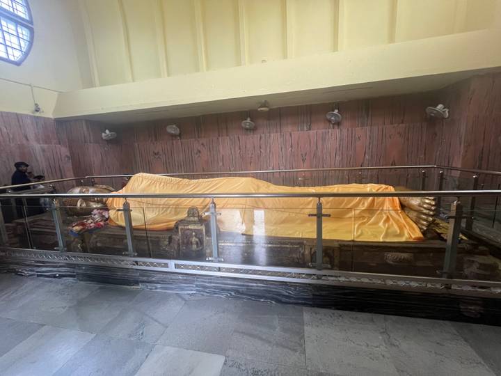 Reclining golden Buddha figure draped in yellow cloth inside a dim hall behind railings.