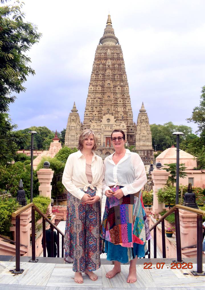 Two women smile in front of the ornate Mahabodhi Temple tower under soft afternoon light.