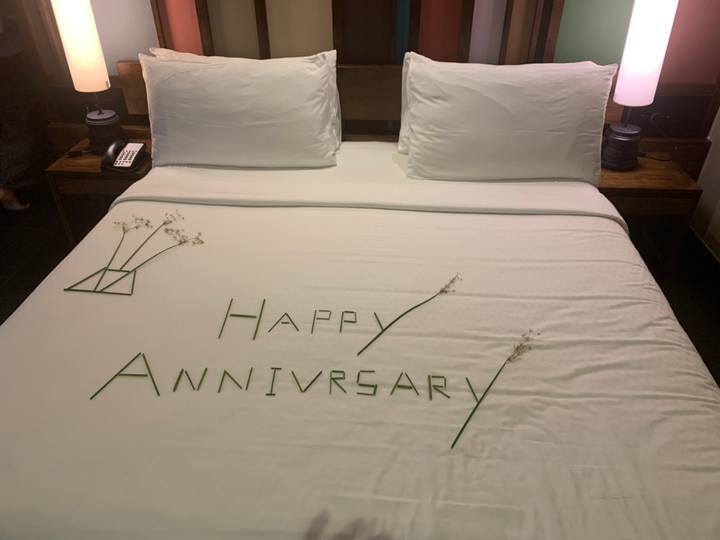 Hotel bed decorated with leaves spelling out 'Happy Anniversary' and small floral accents.