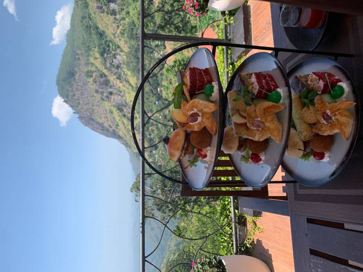 Three-tier stand of pastries and bites set on an outdoor table overlooking lush mountains.