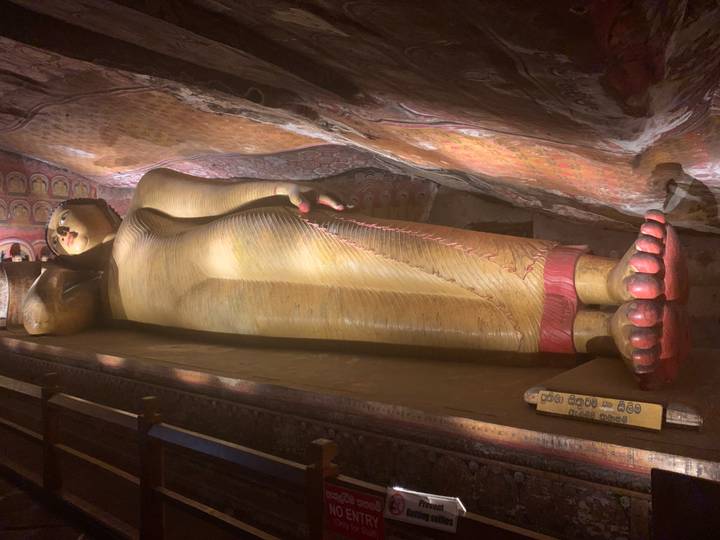 Large golden reclining Buddha statue inside a dimly lit cave temple with painted ceiling.