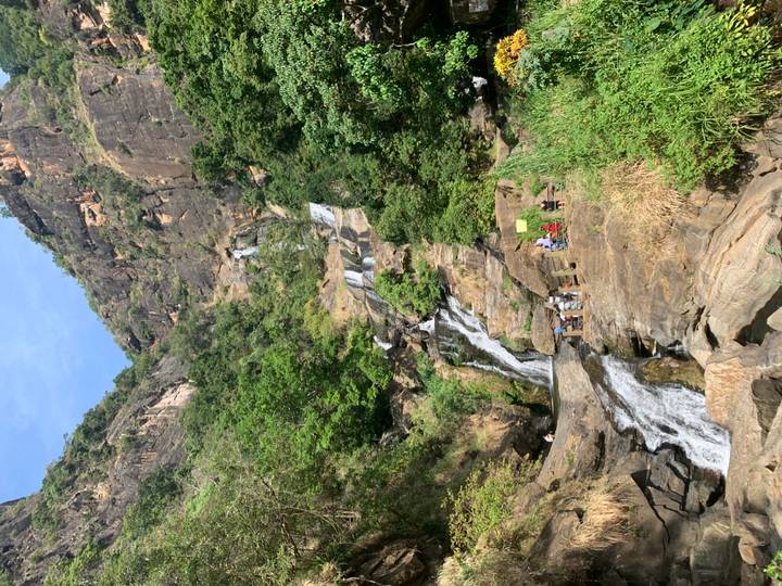 Tall cascading waterfall set in rocky cliffs with visitors gathered at the base.