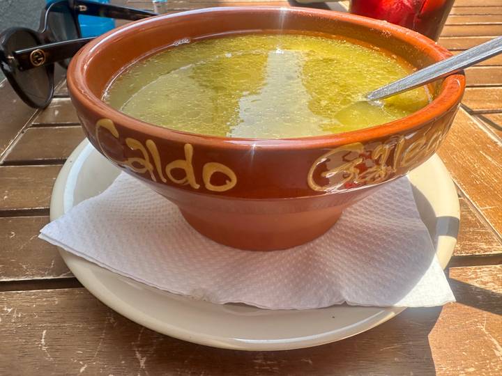 Traditional terracotta bowl of Caldo Gallego soup on an outdoor café table.