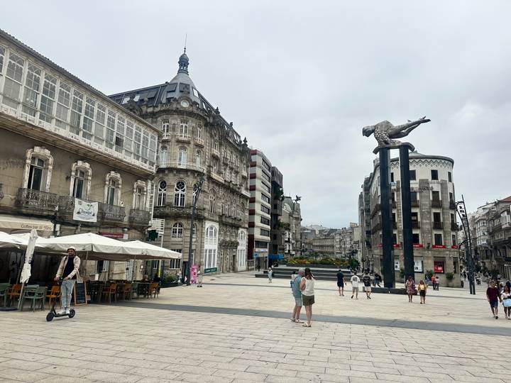 Pedestrian plaza in Vigo featuring historic stone buildings, outdoor cafés, and the modern Sireno sculpture.