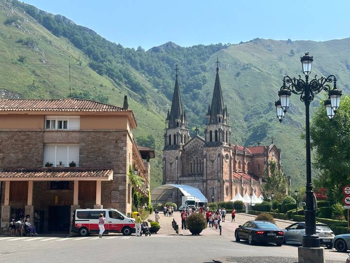 Basilica of Covadonga framed by green mountains with visitors in the foreground on a sunny morning.