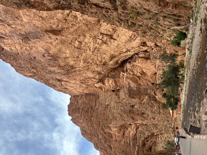 Towering ochre cliffs of Todra Gorge rising above a shallow river and small houses.