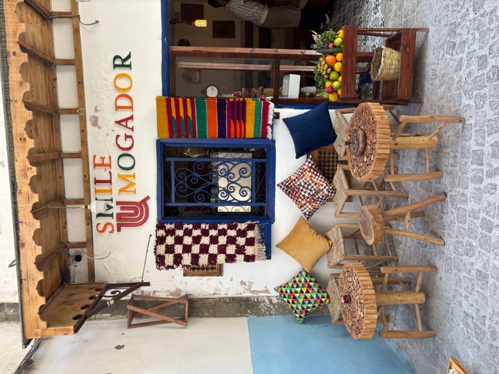 Charming café frontage in Essaouira with woven stools, patterned blankets and fresh fruit display.