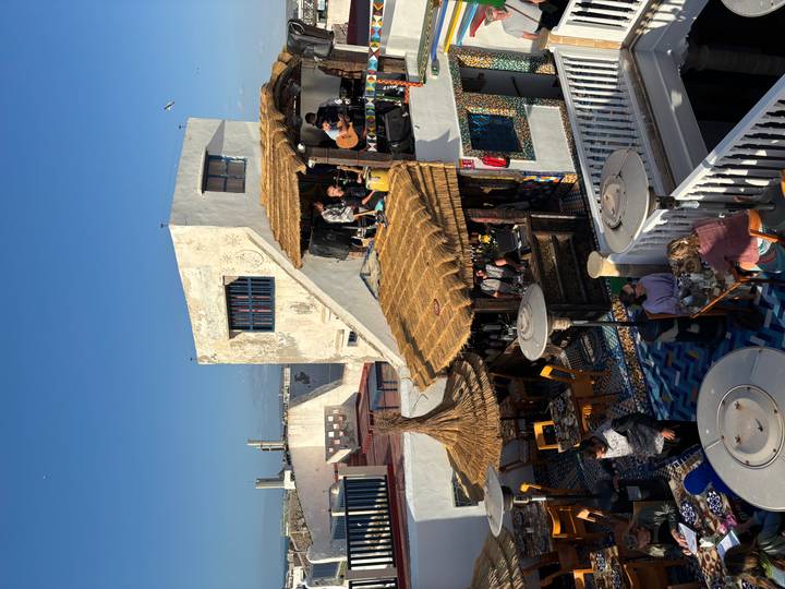 Rooftop restaurant in Essaouira with straw pergolas and diners enjoying ocean views.