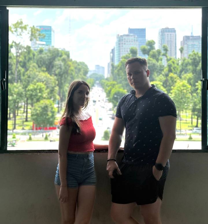 Two visitors stand by a large window overlooking a tree-lined boulevard.