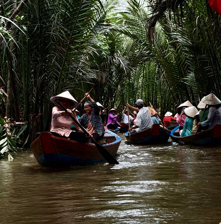 Multiple sampans rowed by locals wearing conical hats through dense nipa palms.