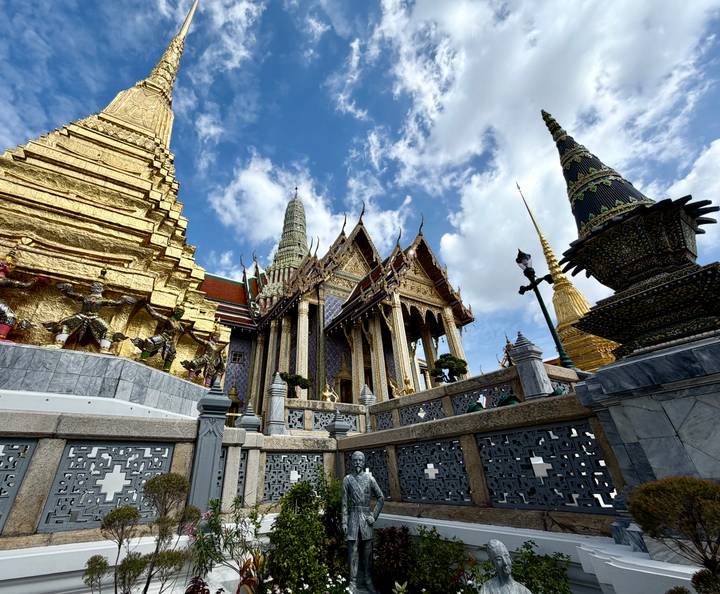 Wide-angle view of gilded stupas and ornate halls at Bangkok's Wat Phra Kaew under blue skies.