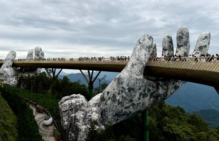 Panoramic view of Da Nang's Golden Bridge held up by giant stone hands over forested hills.