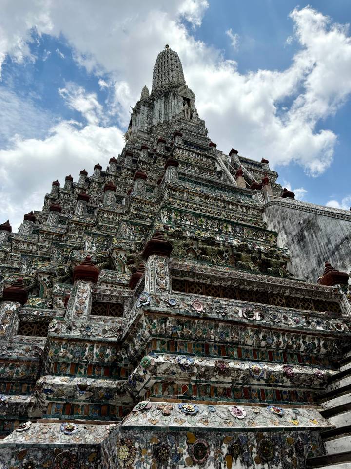 Upward perspective of an ornately tiled temple tower against partly cloudy skies.