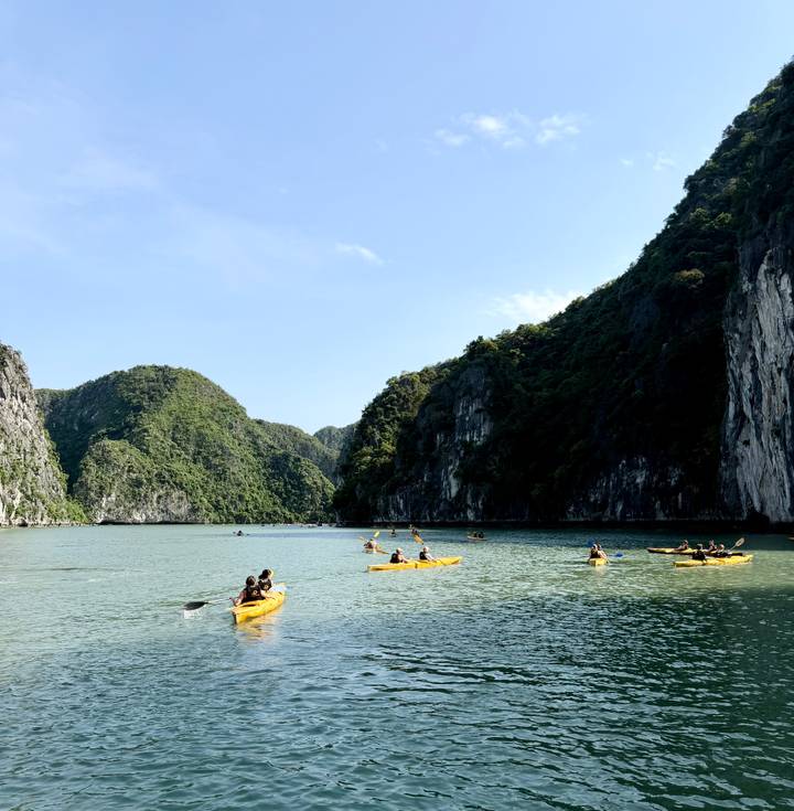 Kayakers paddle through emerald waters surrounded by towering limestone cliffs in Ha Long Bay.