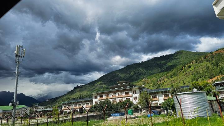 Valley town in Bhutan beneath dark storm clouds with green hills rising behind