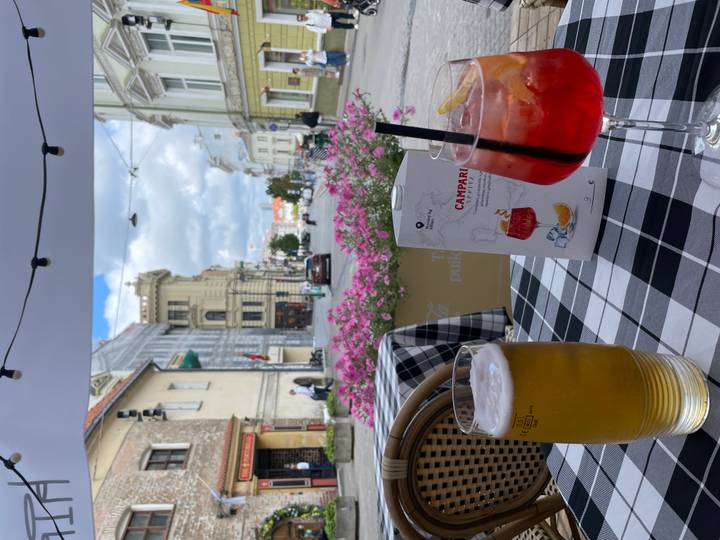 Outdoor café table with beer and Campari spritz overlooking a charming European street and pink flowers