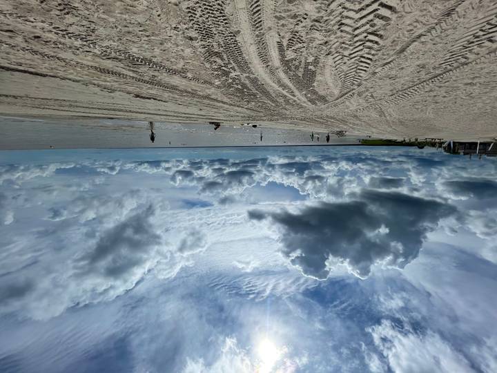 Wide sandy beach with dramatic storm clouds and faint figures near the shoreline