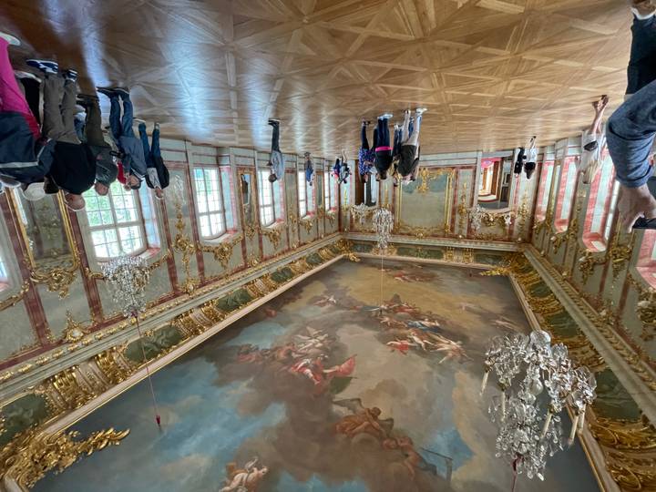 Lavish baroque ballroom with ornate gold details and painted ceiling where tourists admire the decor