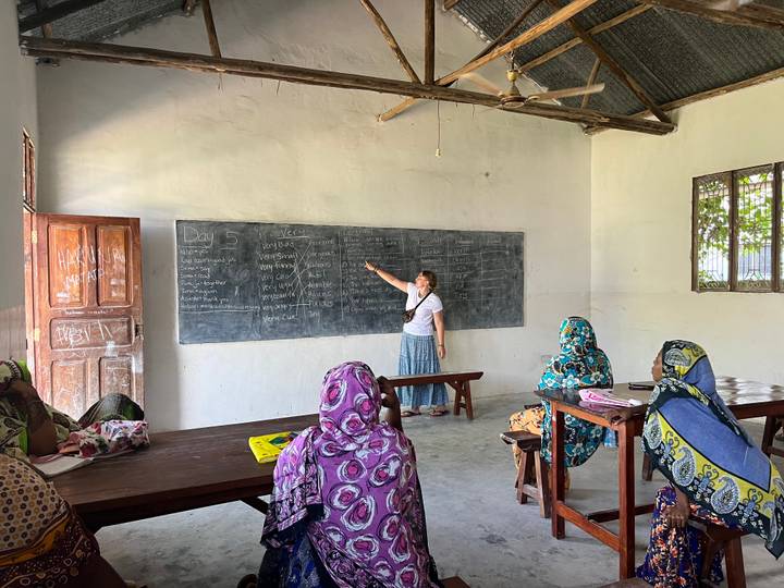 Volunteer teacher points at lessons on a chalkboard while local women listen in a simple classroom