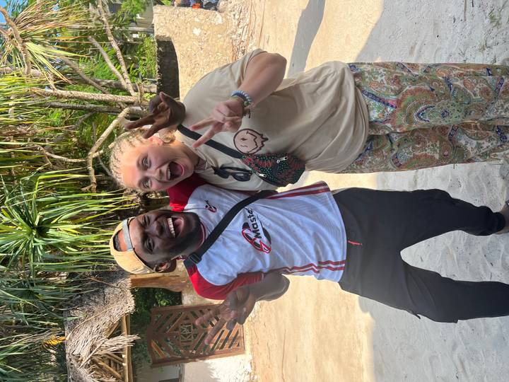 Two friends laugh and pose with peace signs beneath tropical foliage