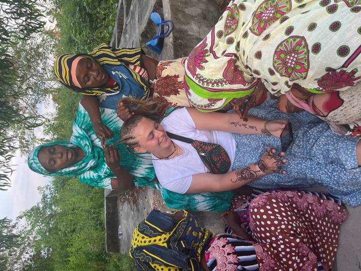 Traveller smiles while local women braid her hair in an outdoor setting