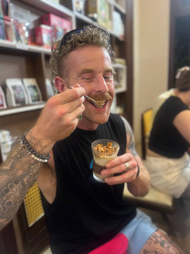 Tattooed traveler enjoys spooning a layered dessert from a glass in a Vietnamese cafe.