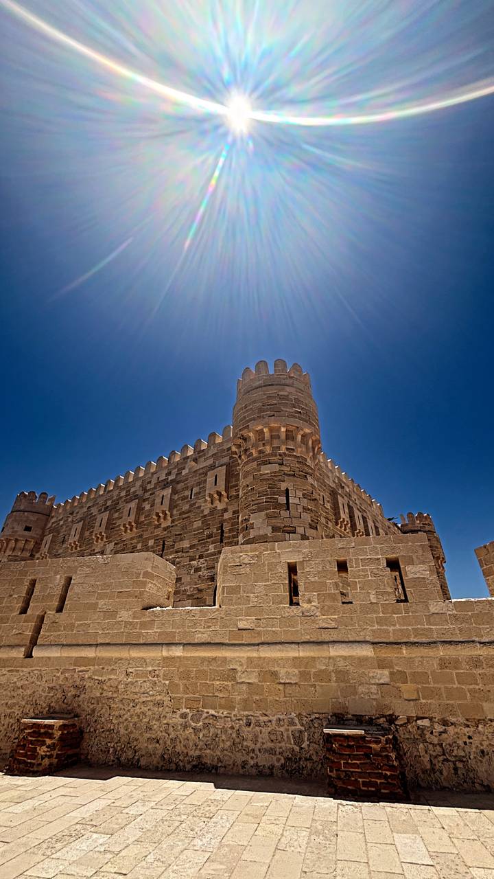 Stone fortress tower under a deep blue sky with sun rays