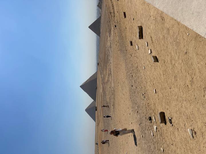Wide desert expanse with three pyramids on the horizon and scattered tourists