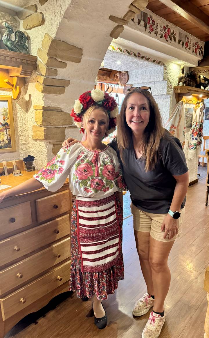 Visitor stands with a woman in ornate Moldovan folk costume inside a rustic restaurant.