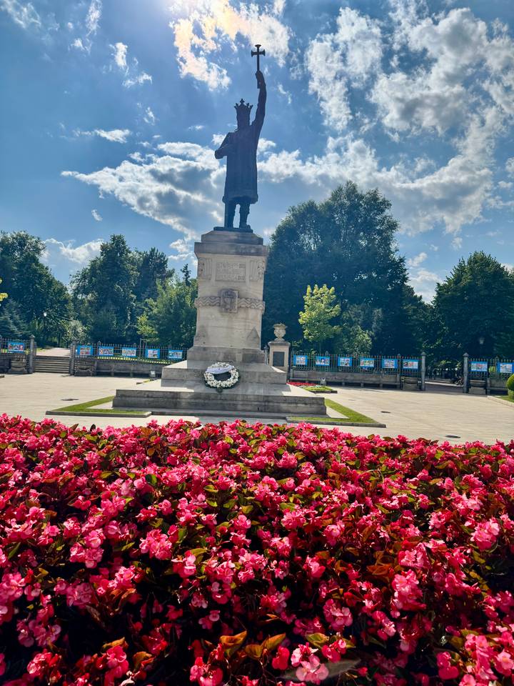 Stone statue on pedestal surrounded by colorful flowerbeds in a city park