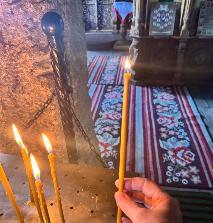 Lit prayer candles in front of a patterned carpet inside an orthodox church