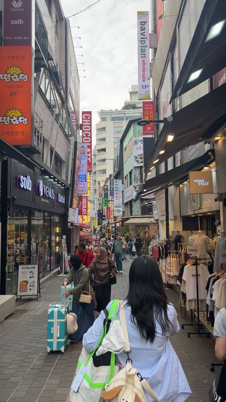 A bustling pedestrian shopping street lined with colorful signs and storefronts in Seoul.