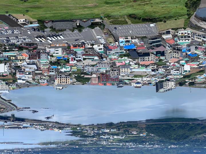 An elevated view shows a coastal town and tranquil blue bay surrounded by hills.