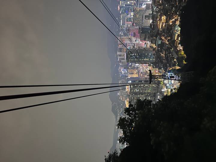 Nighttime city lights sparkle below a cable car line descending a forested hill.