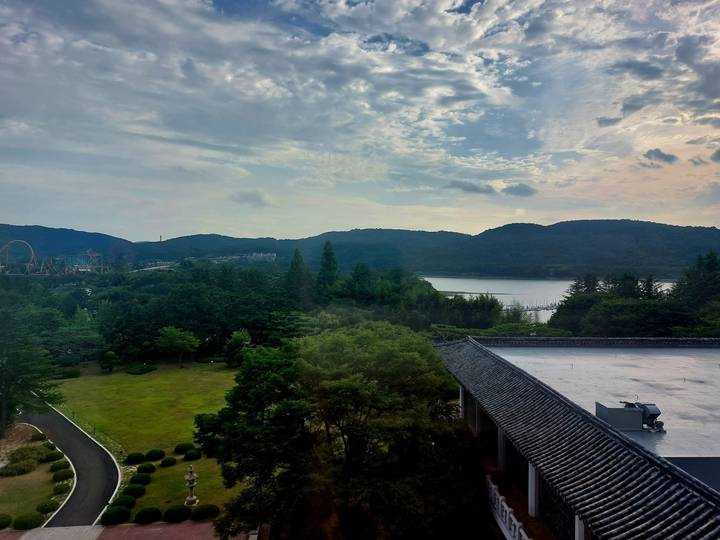 Hazy morning view over a forested park, distant amusement rides and a broad lake backed by low mountains.