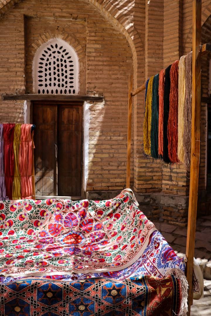 Colorful silk threads and embroidered fabric displayed against old brick walls in a bazaar stall.