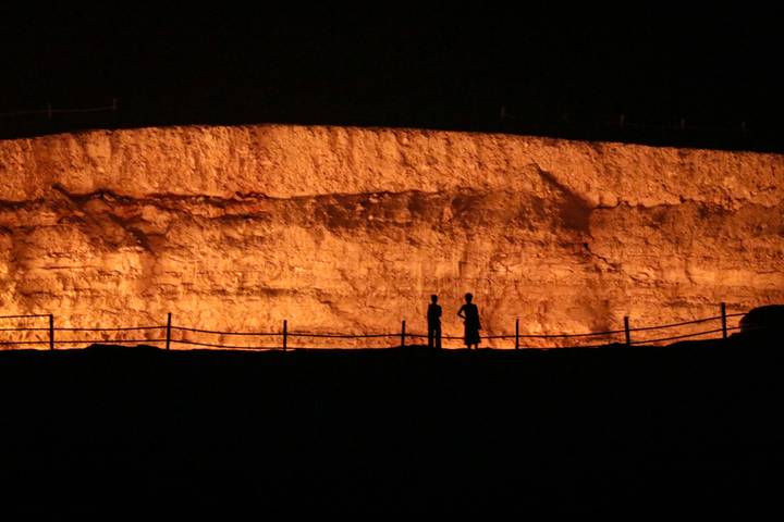 Silhouetted figures stand before a tall, glowing cliff face at night.