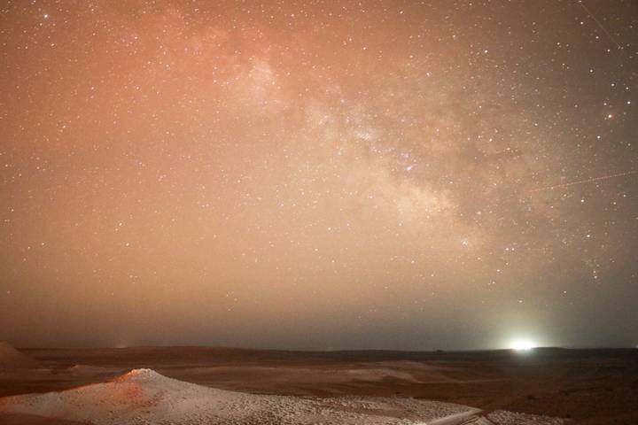 Night sky full of stars over a dark desert horizon with faint Milky Way visible.