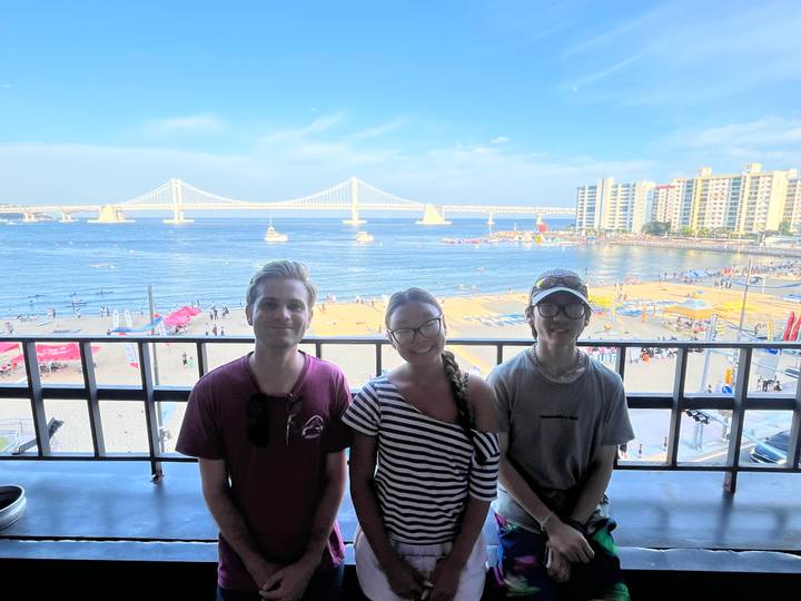 Three travellers pose on a balcony overlooking a busy beach and Gwangan Bridge in Busan.