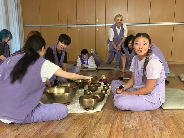 Participants in matching purple attire explore Tibetan singing bowls during an indoor workshop.
