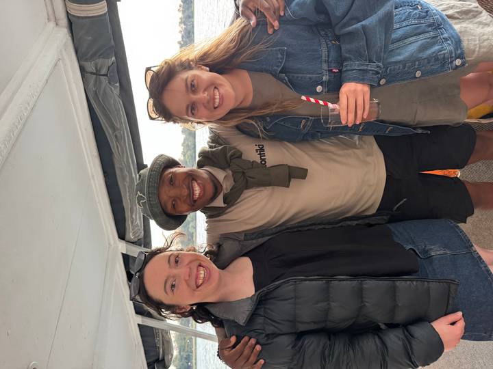 Three smiling travellers posing together on a boat deck, one wearing a Contiki shirt and holding a drink.