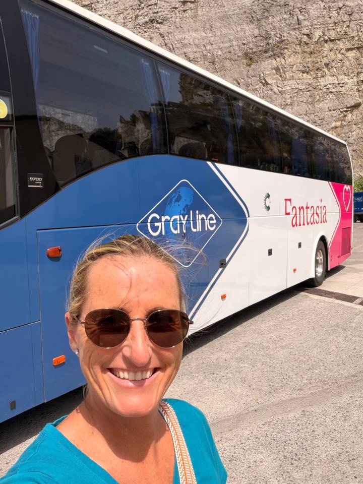 Selfie of woman in sunglasses with Gray Line Fantasia tour bus behind.