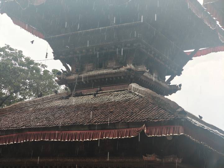 Close-up of a traditional Nepalese temple roof as rain falls heavily against the ornate woodwork.