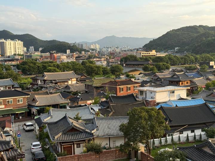 Rooftop view across Jeonju Hanok Village’s traditional tiled houses with distant city and mountain backdrop.