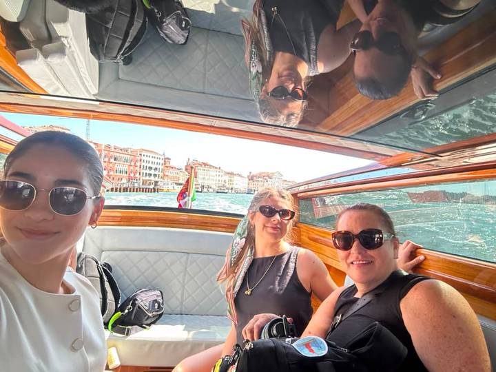 Three friends take a selfie inside a wooden water taxi cruising the Venetian canals.