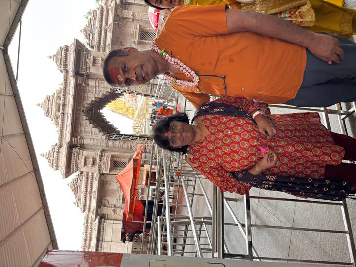 Couple waits inside a queueing area in front of an ornate Indian temple gateway.