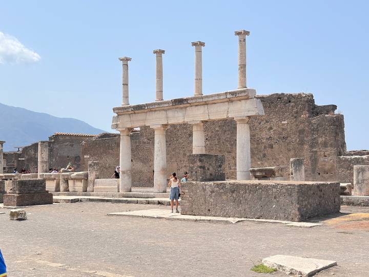 Ancient columns and stone walls in the forum of Pompeii with visitors exploring the ruins.